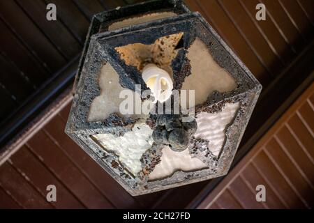 Guardando in alto un vecchio stile Black Metal Light Hanging Da un soffitto di legno marrone scuro Foto Stock