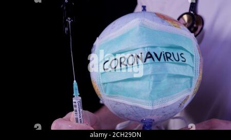 Concetto di epidemia di coronavirus. Globo del mondo con mascherina medica verde su esso. Siringa contenente il medico con il vaccino COVID-19. Mappa del mondo, virus Wuhan Foto Stock