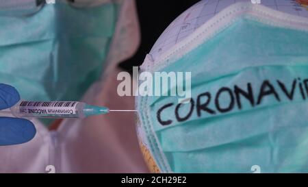 Concetto di vaccino coronavirus COVID-2019. Uomo in uniforme bianca di sicurezza e maschera facendo l'iniezione ad un mondo infettato con coronavirus. Cura per pandemia, Foto Stock