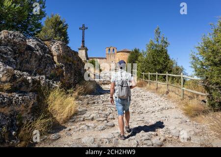 Turista maschile a piedi verso una chiesa romanica Ermita de San Frutos. Hermitage sulla cima di una collina tra le scogliere. Casa di grifone avvoltoi. Hoces del Du Foto Stock