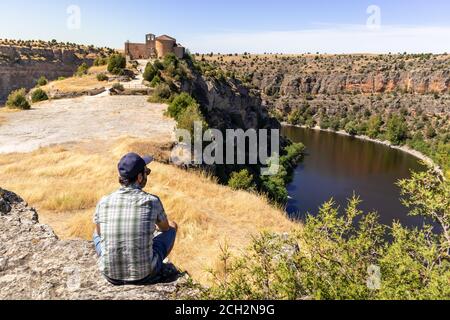 Posti a sedere per turisti maschili della chiesa romanica Ermita de San Frutos. Hermitage sulla cima di una collina tra le scogliere. Casa di grifone avvoltoi. Panoramica. Hoces de Foto Stock