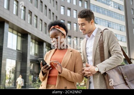 Giovane uomo d'affari sorridente che guarda lo schermo dello smartphone nelle mani di collega Foto Stock