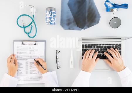 Vista dall'alto delle mani di giovani medici in whitecoats fare note mediche e digitazione Foto Stock