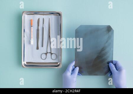 Vista delle mani gugorate del chirurgo che mette l'immagine radiografica vicino strumenti medici Foto Stock