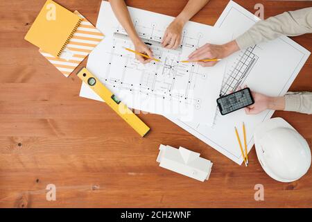 Vista dall'alto delle mani di due architetti che indicano il modello durante la discussione Foto Stock