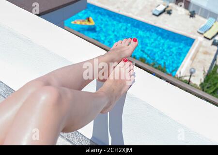 Bella donna gambe seduta su sedia sulla terrazza bianca di villa hotel resort con vista piscina Foto Stock