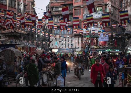 Kathmandu, Nepal - Dicembre 22 2019:persone non identificate cammina e guida da diversi negozi e venditori di strada sulla strada con bandiere colorate sopra Foto Stock