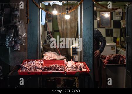 Kathmandu, Nepal - Dicembre 22: Un macellaio maschile non identificato prepara e vende carne cruda in contenitori di plastica rossa sotto due lampadine sulla strada Foto Stock