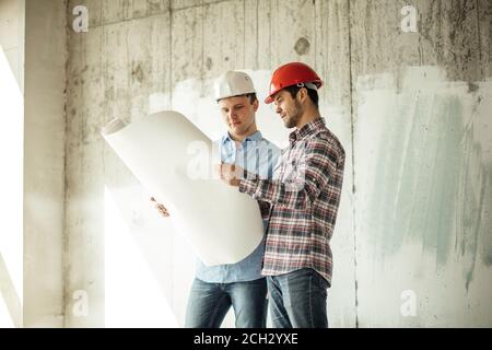 ingegnere creativo di talento sta mostrando il piano di oggetto ad un cliente nella casa che è in costruzione. vista laterale foto. copyspace Foto Stock