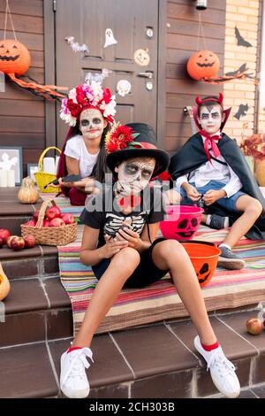 Ragazzo cupo con faccia dipinta seduta contro i suoi amici dentro costumi di halloween Foto Stock