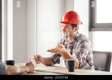 bell'ingegnere in rosso hardhat sta offrendo il lavoro a un uomo. primo piano foto. Foto Stock