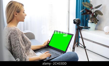 Blogger donna che lavora su un computer portatile. Vista della fotocamera su treppiede e laptop con schermo verde chromakey Foto Stock