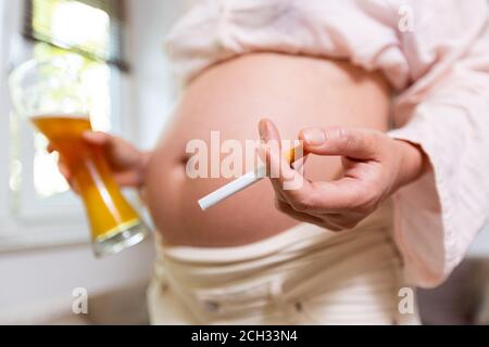una donna incinta con una birra e una sigaretta dentro la sua mano Foto Stock