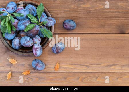 Alcune prugne blu mature lavate con foglie in un piatto marrone sul tavolo di legno. Diverse ossa giacciono separatamente. Spazio di copia. La vista dall'alto Foto Stock