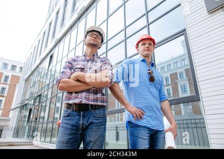 costruttori impressionanti sicuri in vestiti casual stanno posando alla macchina fotografica davanti all'edificio. realizzatori nel commercio Foto Stock