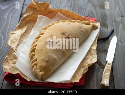 Pizza italiana calzone con funghi, spinaci e formaggio su una superficie di legno, stile rustico, fuoco selettivo Foto Stock