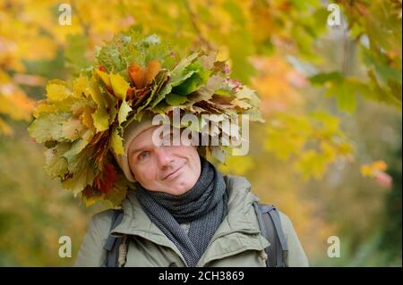 Uomo in corona d'autunno con foglie rosse e arancioni che guardano alla fotocamera Foto Stock