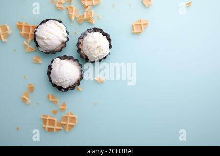 Vista dall'alto delle palle di gelato alla vaniglia nei waffle e. ciotola di cioccolato su sfondo blu Foto Stock