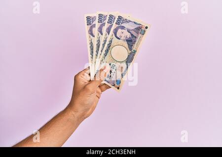 Mano ispanica che tiene 5000 yen giapponesi su sfondo rosa isolato. Foto Stock