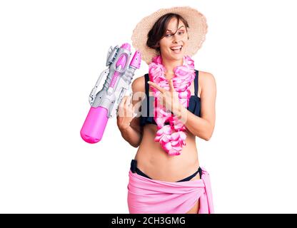 Bella giovane donna con capelli corti indossando bikini e hawaiano lei tenendo una pistola ad acqua sorridente felice indicando con la mano e. dito Foto Stock