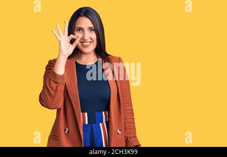 Giovane bella donna bruna con abiti eleganti sorridente positivo facendo ok segno con mano e dita. Espressione riuscita. Foto Stock