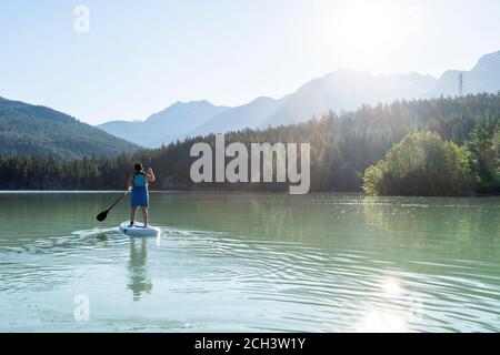 Anonimo femmina paddleboarding in giornata di sole sul lago di montagna Foto Stock