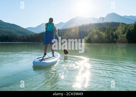 Anonimo femmina paddleboarding in giornata di sole sul lago di montagna Foto Stock