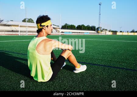 giovane ragazzo in abbigliamento sportivo guarda l'orizzonte seduto l'erba Foto Stock