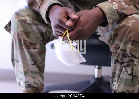 Mani di un medico militare nero che tiene una maschera chirurgica durante la pandemia COVID-19. STATI UNITI. Foto Stock