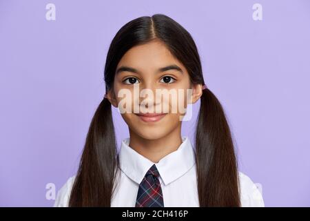 Sorridente ragazza indiana bambino indossare scuola uniforme stand su sfondo lilla, ritratto. Foto Stock