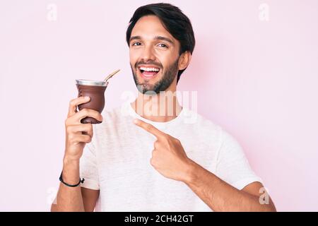 Bell'uomo ispanico bere compagno infusione sorridente felice indicando con mano e dito Foto Stock