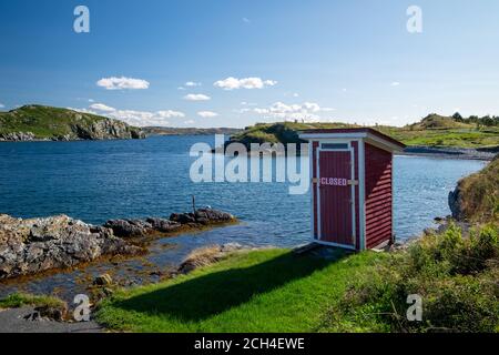 Un piccolo edificio rosso, all'esterno, sul bordo di una scogliera rocciosa con oceano blu e isole sullo sfondo. Foto Stock