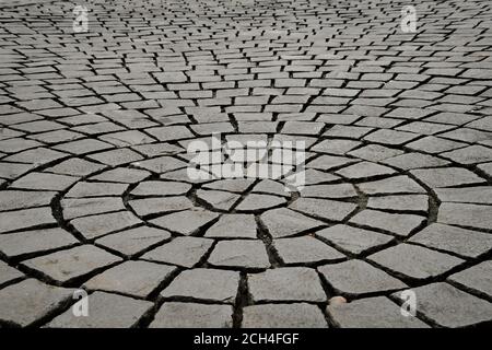 Una vista prospettica a livello del suolo di ciottoli di pavimentazione in pietra grigia in un disegno di cerchi concentrici crescenti. Foto Stock