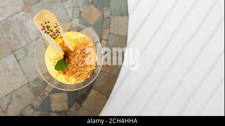 elegante bicchiere con dessert in mousse gialla, biscotti e topping su tavola rotonda, banner di grande formato, fuoco selettivo Foto Stock