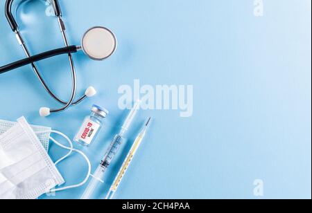 Concetto sanitario e medico. Stetoscopio con maschera protettiva per iniezione o maschera medica e vaccino su sfondo blu. Proteggere Coronav Foto Stock