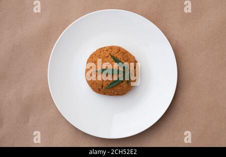 Foglia di cannabis con biscotti su un piatto bianco. Estrazione di resina viva di cannabis su sfondo kraft. Foto Stock