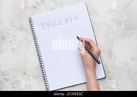 Donna che scrive la parola DISLESSIA in taccuino su sfondo chiaro Foto Stock