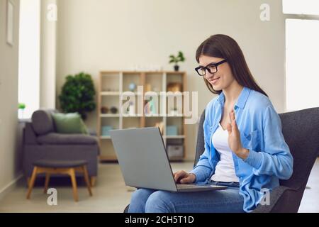 Giovane donna in occhiali che fa videochiamata su laptop e. lancetta per salutare parenti o colleghi Foto Stock