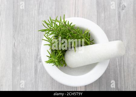 Rosmarino in un pestello e mortaio di granito bianco. Sfondo di legno grigio Foto Stock