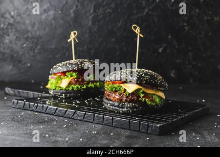 Gustosi hamburger con panino nero su sfondo scuro Foto Stock