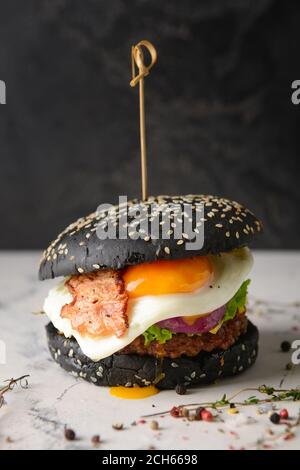 Gustoso hamburger con panino nero sul tavolo Foto Stock