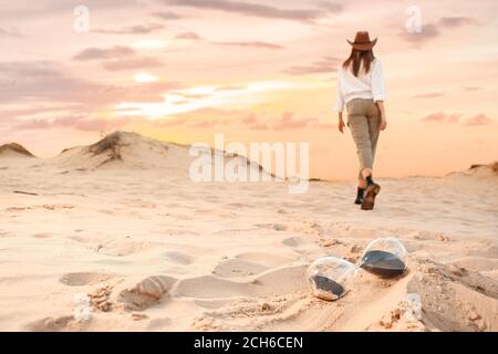 Clessidra sulla sabbia e donna che cammina nel deserto Foto Stock