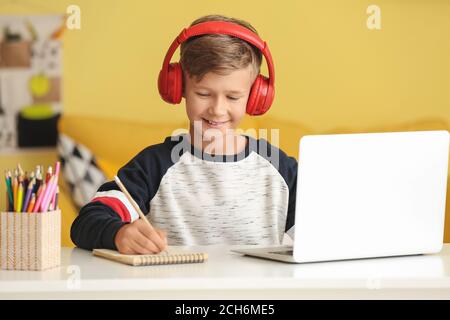 Piccolo ragazzo con le cuffie che fa le lezioni a casa Foto Stock