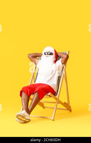 Babbo Natale afroamericano seduto sul lettino da sole su sfondo colorato Foto Stock