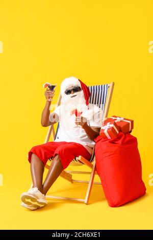 Babbo Natale afroamericano seduto sul lettino da sole su sfondo colorato Foto Stock
