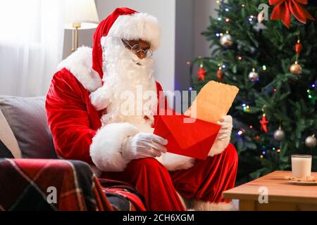 Lettera di lettura afroamericana di Babbo Natale in camera decorata per Natale Foto Stock