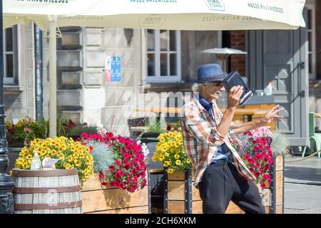 Gdansk, North Poland - August 14, 2020: An old man with blue hat dressed up as hip hop trendy clothing listening to radio and performing dance for liv Stock Photo