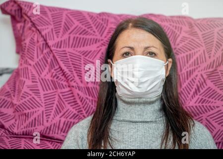 Donna nel letto di casa che indossa la maschera con i sintomi del coronavirus. Foto Stock