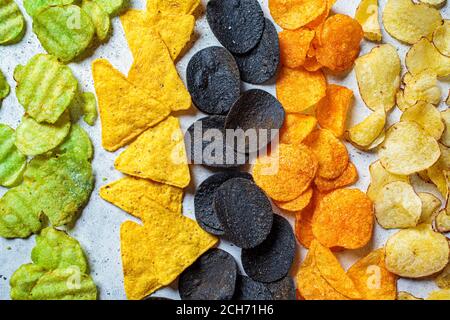 Diversi tipi di patatine colorate, sfondo grigio. Concetto di fast food, alimenti grassi carboidrati malsani. Foto Stock