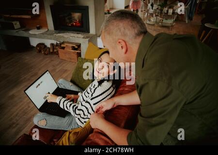 Vista ad alto angolo della donna che chiede consiglio dal marito mentre navighi nei siti di shopping su un computer portatile a casa Foto Stock